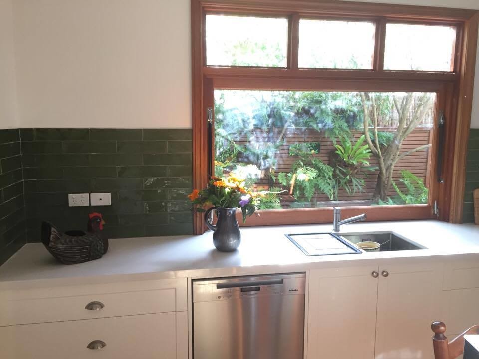 Photo of a mid-sized country u-shaped eat-in kitchen in Melbourne with a single-bowl sink, shaker cabinets, white cabinets, granite benchtops, green splashback, ceramic splashback, stainless steel appliances, light hardwood floors and white benchtop.