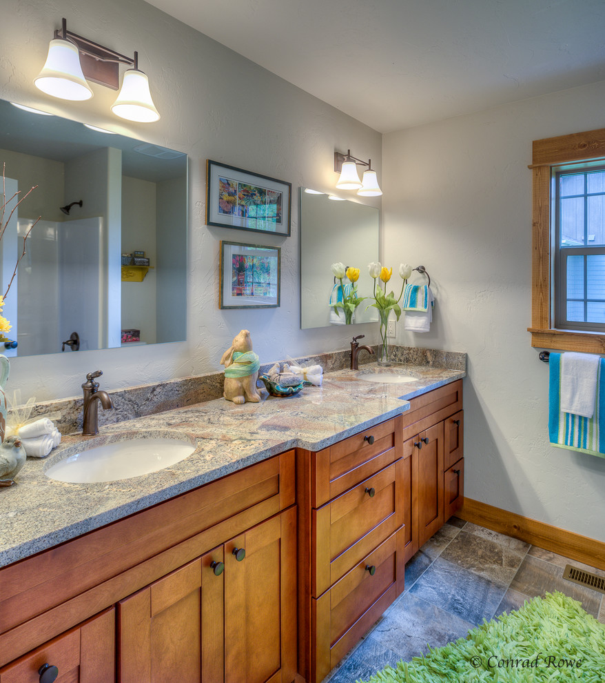 This is an example of a mid-sized country kids bathroom in Other with recessed-panel cabinets, medium wood cabinets, a shower/bathtub combo, a one-piece toilet, multi-coloured tile, ceramic tile, white walls, ceramic floors, an undermount sink and granite benchtops.