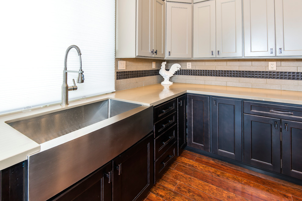 Large transitional l-shaped medium tone wood floor kitchen photo with a farmhouse sink, brown cabinets, granite countertops, beige backsplash, subway tile backsplash, stainless steel appliances, an island and recessed-panel cabinets