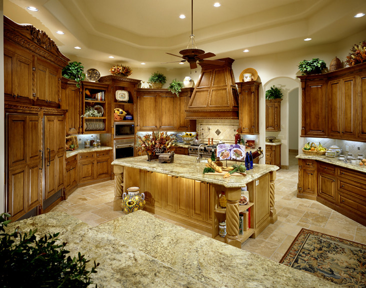 Photo of an expansive mediterranean u-shaped eat-in kitchen in Phoenix with a farmhouse sink, recessed-panel cabinets, medium wood cabinets, granite benchtops, beige splashback, mosaic tile splashback, panelled appliances, travertine floors and with island.