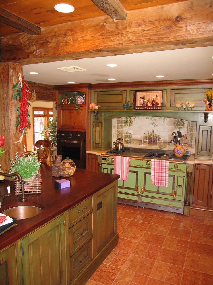 Photo of a mid-sized country u-shaped kitchen in Newark with a farmhouse sink, beaded inset cabinets, green cabinets, copper benchtops, orange splashback, porcelain splashback, terra-cotta floors and with island.