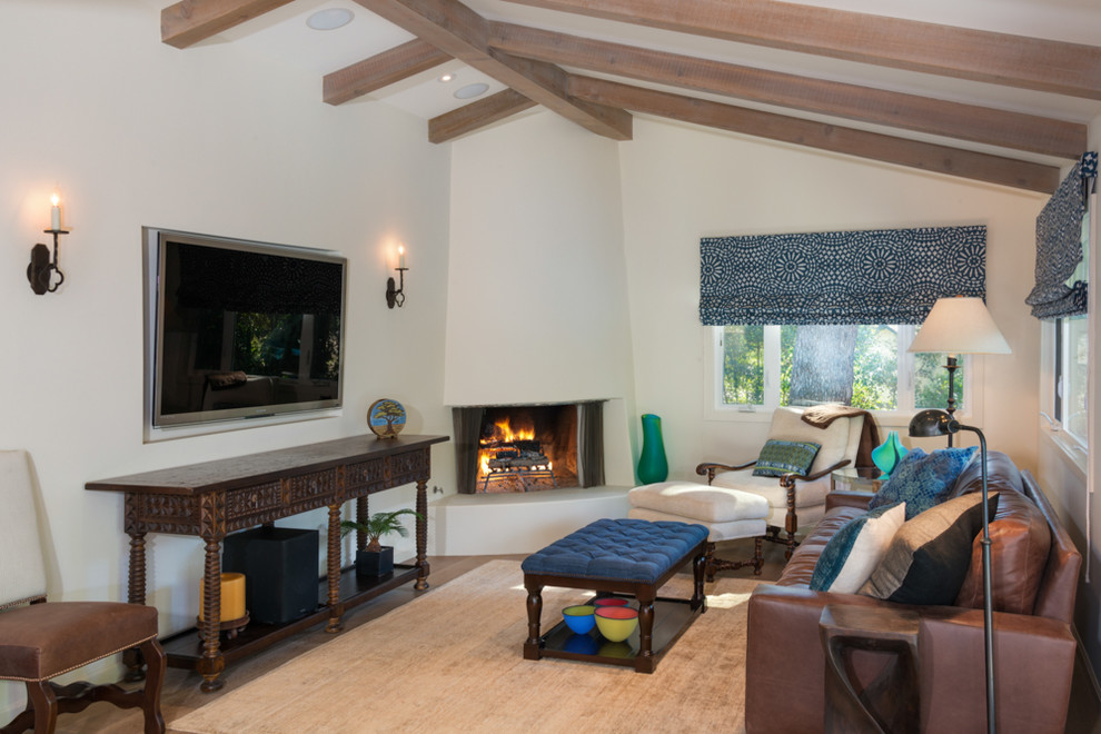 This is an example of a mediterranean family room in Los Angeles with white walls, a corner fireplace and a wall-mounted tv.