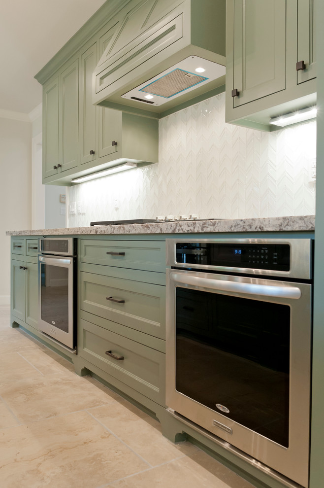 Kitchen - large tropical galley porcelain tile kitchen idea in Houston with a farmhouse sink, recessed-panel cabinets, green cabinets, granite countertops, white backsplash, glass tile backsplash, stainless steel appliances and an island