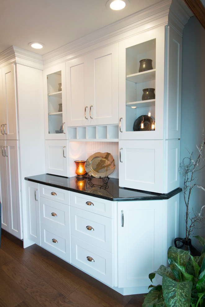 Example of a large transitional l-shaped medium tone wood floor eat-in kitchen design with an undermount sink, shaker cabinets, white cabinets, granite countertops, gray backsplash, stone tile backsplash, stainless steel appliances and an island