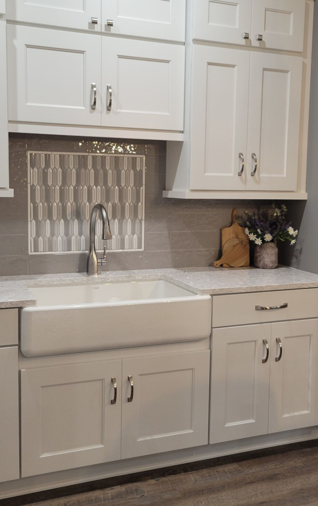 Mid-sized transitional galley vinyl floor and brown floor kitchen photo with a farmhouse sink, recessed-panel cabinets, white cabinets, quartz countertops, gray backsplash, ceramic backsplash and white countertops