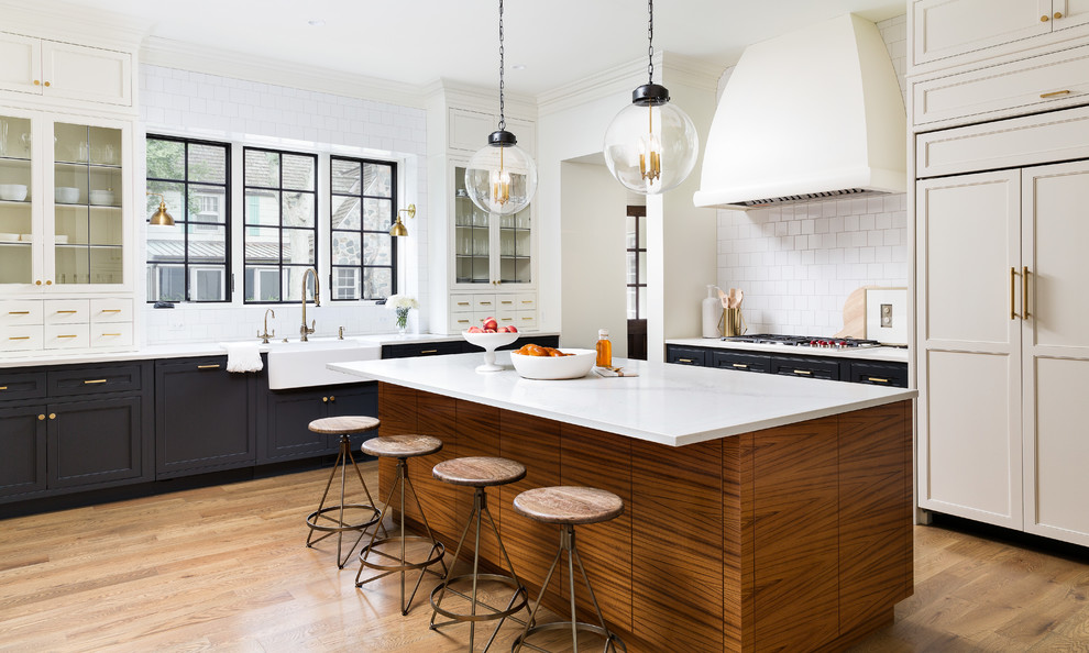 Inspiration for a large transitional l-shaped eat-in kitchen in Detroit with with island, a farmhouse sink, shaker cabinets, blue cabinets, white splashback, panelled appliances, medium hardwood floors, brown floor and white benchtop.