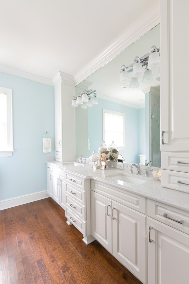 This is an example of a mid-sized contemporary 3/4 bathroom with shaker cabinets, white cabinets, an alcove shower, a one-piece toilet, blue walls, medium hardwood floors, an undermount sink, brown floor, a hinged shower door and white benchtops.