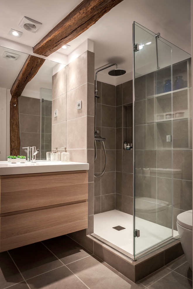Photo of a mid-sized modern 3/4 wet room bathroom in Bilbao with flat-panel cabinets, light wood cabinets, a wall-mount toilet, gray tile, ceramic tile, grey walls, ceramic floors, an integrated sink and solid surface benchtops.