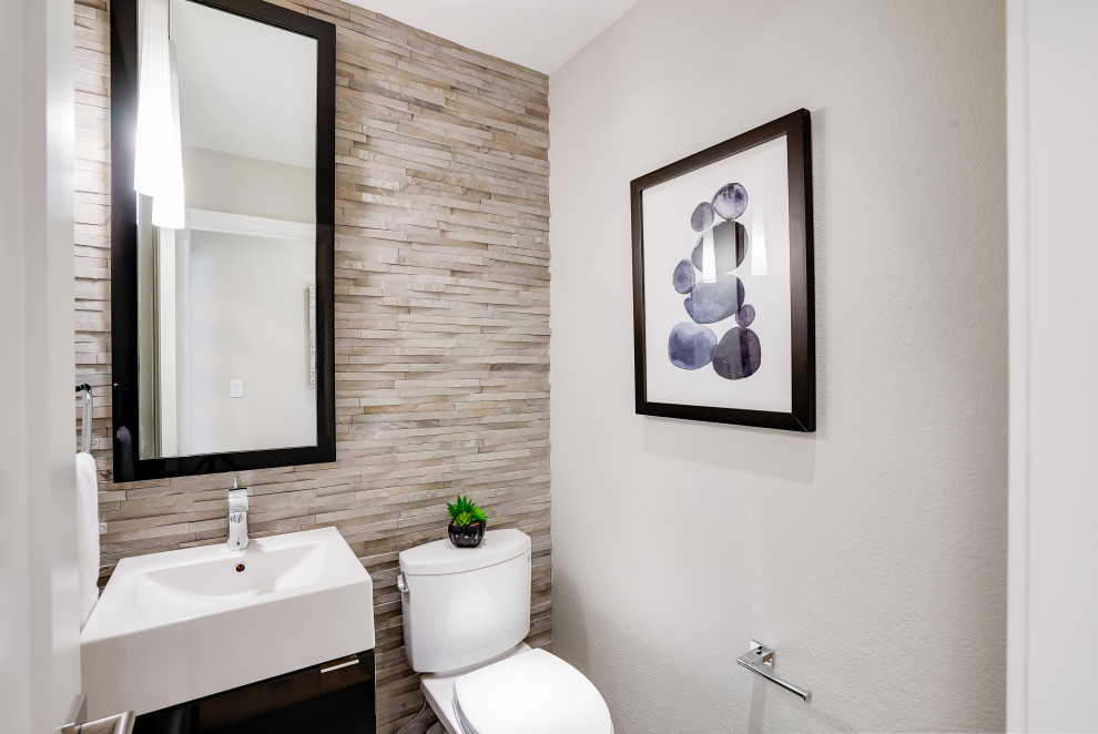 Cette image montre un petit WC et toilettes minimaliste avec un placard à porte plane, des portes de placard noires, WC à poser, un carrelage beige, un carrelage de pierre, un mur blanc, un lavabo intégré et meuble-lavabo suspendu.