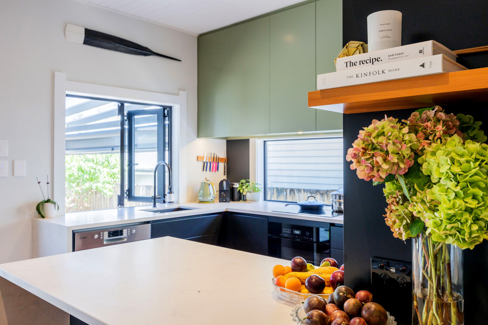 Small modern eat-in kitchen in Auckland with an undermount sink, solid surface benchtops, black splashback, medium hardwood floors, a peninsula and grey benchtop.