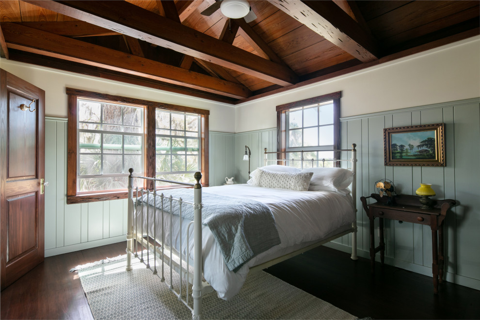 Mittelgroßes Country Hauptschlafzimmer ohne Kamin mit blauer Wandfarbe, dunklem Holzboden, freigelegten Dachbalken und Holzwänden in Tampa