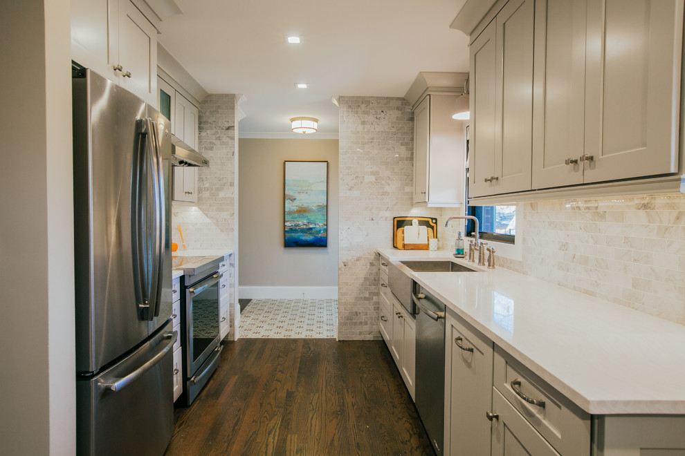 Photo of a large transitional galley separate kitchen in Denver with a farmhouse sink, shaker cabinets, grey cabinets, quartz benchtops, white splashback, marble splashback, stainless steel appliances, medium hardwood floors, a peninsula, brown floor and white benchtop.