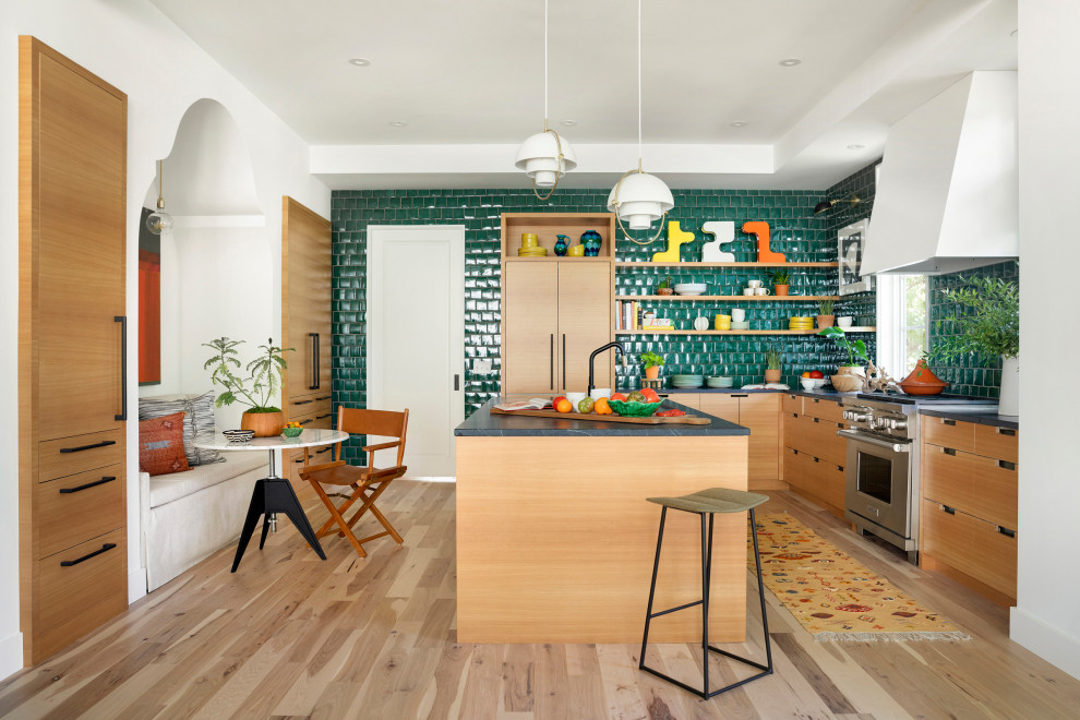 Photo of a large eclectic l-shaped eat-in kitchen in Minneapolis with flat-panel cabinets, light wood cabinets, soapstone benchtops, with island, green splashback, glass tile splashback, panelled appliances, light hardwood floors, grey floor and grey benchtop.