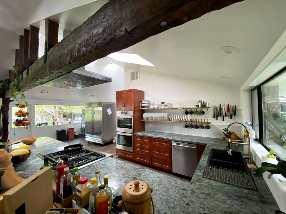 Photo of a mid-sized beach style u-shaped eat-in kitchen in San Francisco with a drop-in sink, shaker cabinets, brown cabinets, granite benchtops, white splashback, ceramic splashback, stainless steel appliances, vinyl floors, a peninsula, brown floor, green benchtop and vaulted.