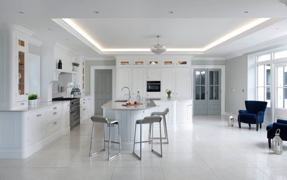 Large classic l-shaped open plan kitchen in Belfast with a submerged sink, beaded cabinets, white cabinets, quartz worktops, grey splashback, stone slab splashback, stainless steel appliances, porcelain flooring, an island and grey floors.