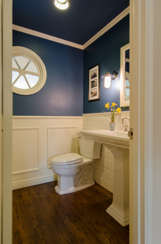 Photo of a small traditional powder room in Seattle with white tile, blue walls, a pedestal sink, subway tile, dark hardwood floors and brown floor.