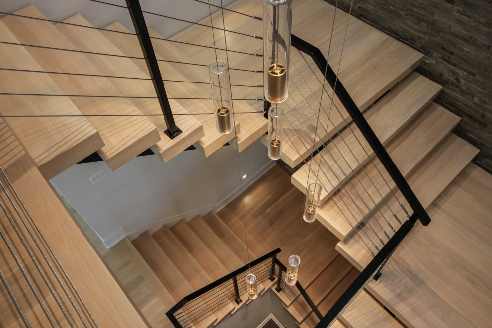 Aménagement d'un grand escalier flottant éclectique avec des marches en bois, un garde-corps en métal et un mur en parement de brique.