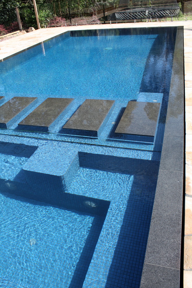 Photo of a large modern backyard rectangular pool in Melbourne with natural stone pavers.