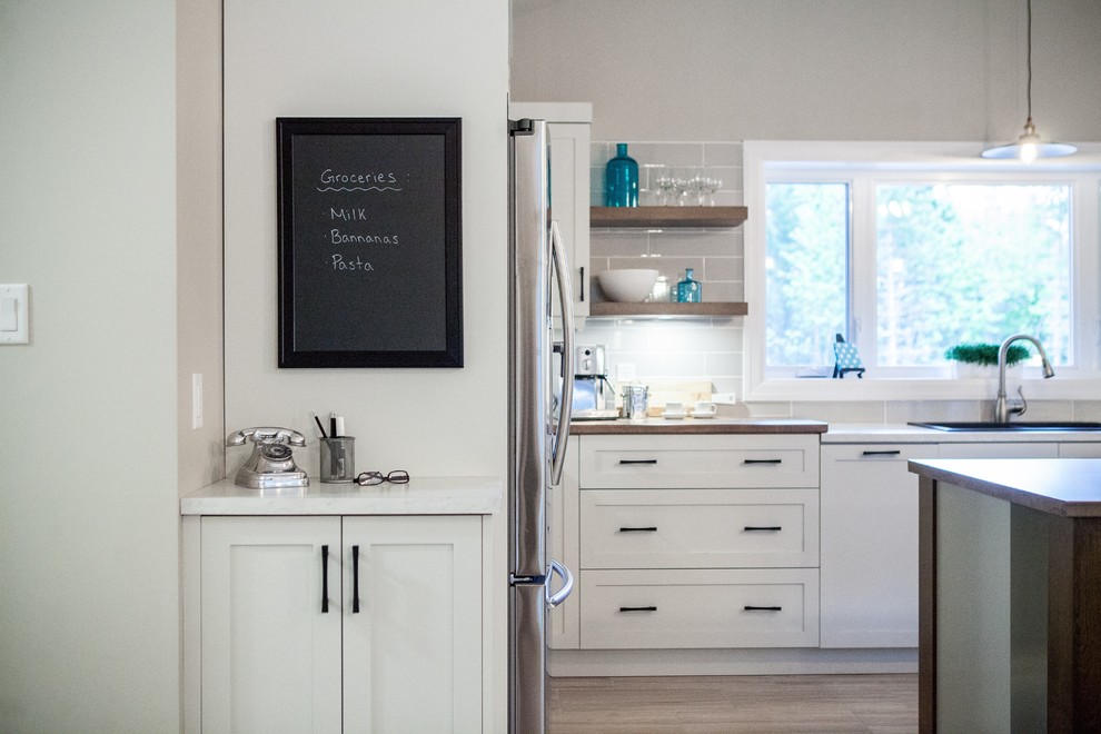 Example of a mid-sized minimalist u-shaped medium tone wood floor and brown floor open concept kitchen design with a drop-in sink, shaker cabinets, white cabinets, quartz countertops, gray backsplash, ceramic backsplash, stainless steel appliances, an island and white countertops