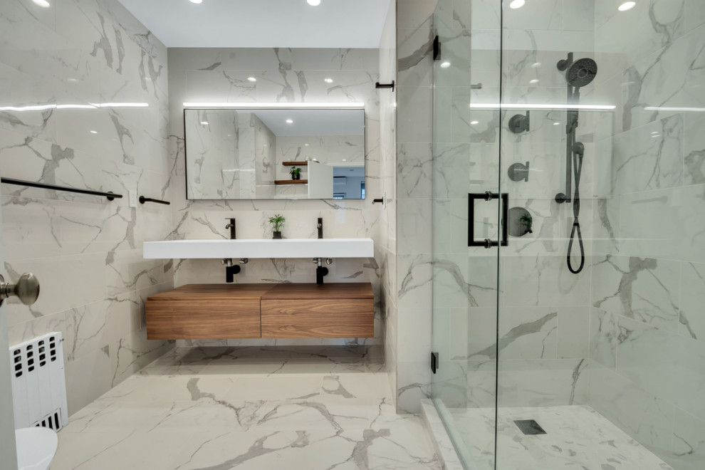 Inspiration for a large modern master bathroom in New York with flat-panel cabinets, brown cabinets, a drop-in tub, a shower/bathtub combo, a bidet, multi-coloured tile, porcelain tile, white walls, porcelain floors, a pedestal sink, limestone benchtops, white floor, a hinged shower door, white benchtops, a niche, a double vanity and a floating vanity.