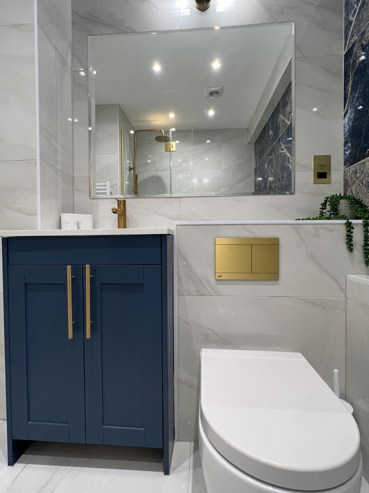 Design ideas for a mid-sized modern bathroom in London with shaker cabinets, blue cabinets, a drop-in tub, an alcove shower, a wall-mount toilet, blue tile, porcelain tile, white walls, porcelain floors, an integrated sink, quartzite benchtops, white floor, an open shower, white benchtops, a single vanity and a freestanding vanity.