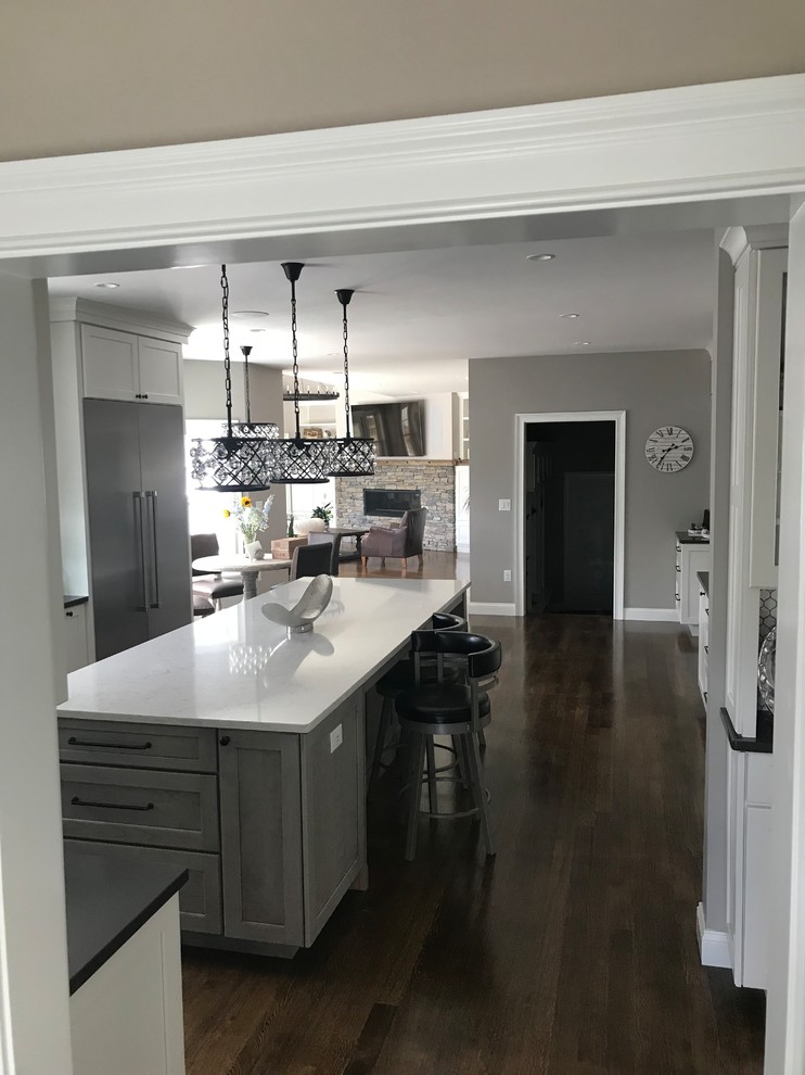 This is an example of a mid-sized traditional u-shaped kitchen in Boston with shaker cabinets, white cabinets, quartz benchtops, stainless steel appliances, dark hardwood floors, with island, brown floor and white benchtop.