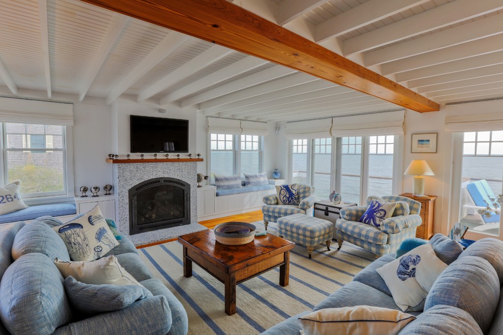 Photo of a beach style living room in Boston with white walls, medium hardwood floors, a standard fireplace, a tile fireplace surround and a wall-mounted tv.