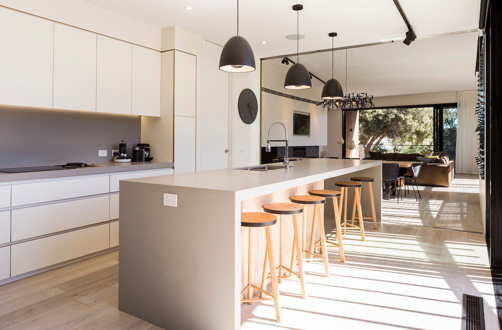 Inspiration for a contemporary galley kitchen in Other with a double-bowl sink, flat-panel cabinets, white cabinets, grey splashback, light hardwood floors, with island, beige floor and grey benchtop.