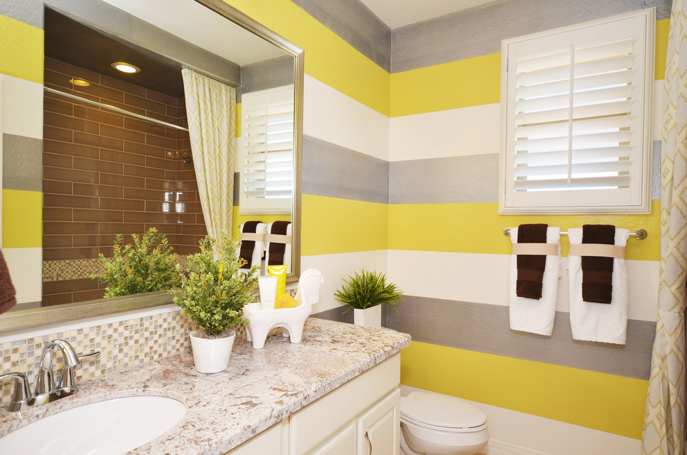 Inspiration for a mid-sized traditional kids bathroom in Phoenix with a drop-in sink, raised-panel cabinets, white cabinets, engineered quartz benchtops, a drop-in tub, a shower/bathtub combo, a one-piece toilet, gray tile, porcelain tile, yellow walls and porcelain floors.