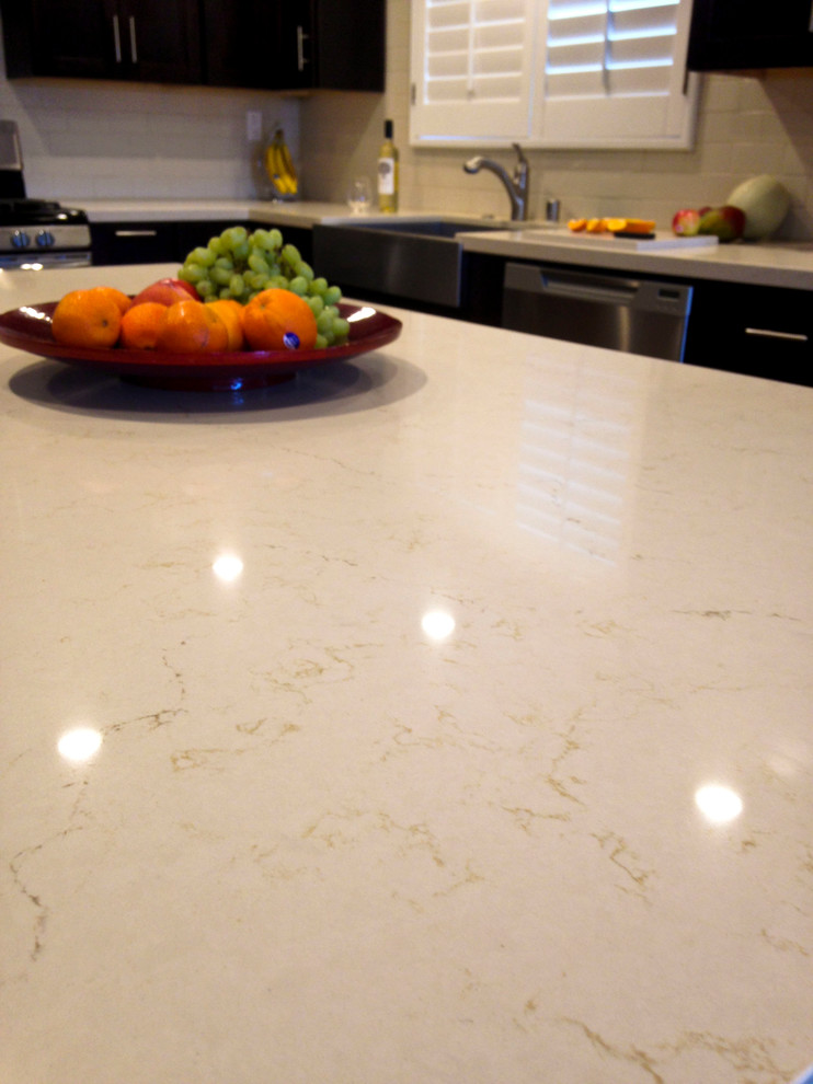 Example of a transitional kitchen design in Los Angeles with a farmhouse sink, shaker cabinets, dark wood cabinets, quartz countertops, beige backsplash, subway tile backsplash, stainless steel appliances and an island