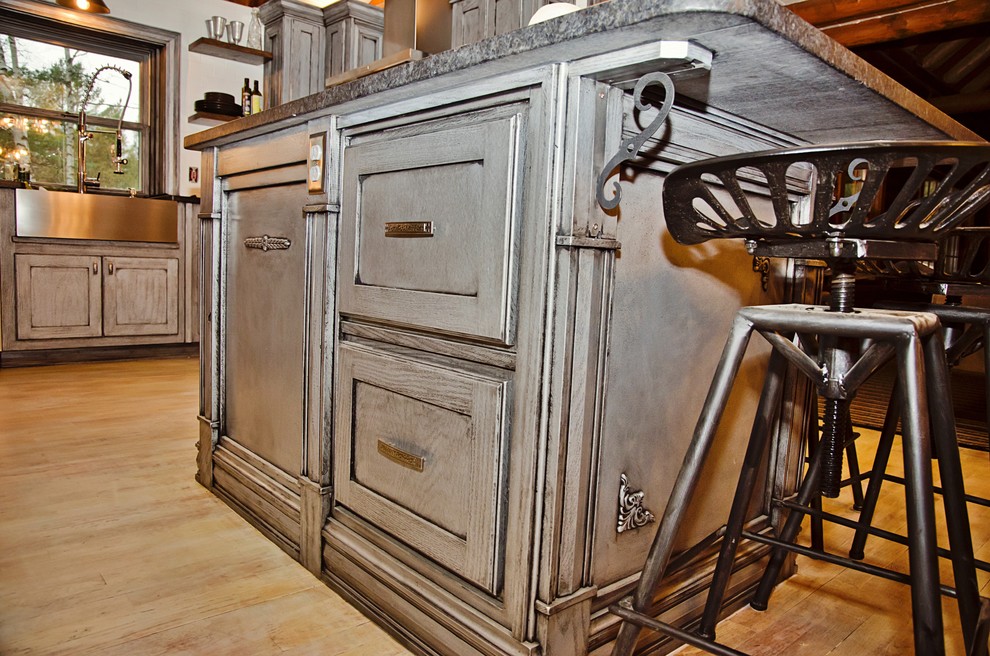 Example of a mid-sized arts and crafts u-shaped light wood floor and white floor eat-in kitchen design with a farmhouse sink, recessed-panel cabinets, gray cabinets, granite countertops, white backsplash, cement tile backsplash, stainless steel appliances and an island