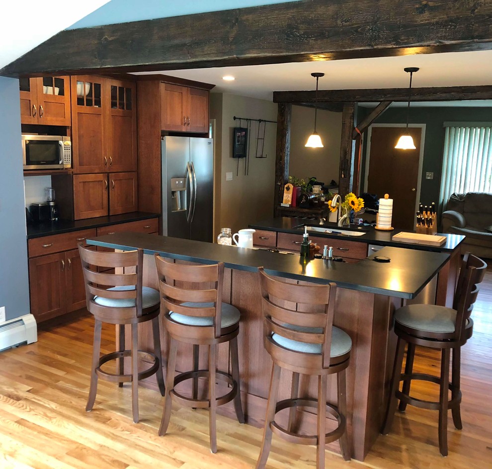 Design ideas for an arts and crafts galley eat-in kitchen in Portland Maine with an undermount sink, shaker cabinets, brown cabinets, granite benchtops, white splashback, subway tile splashback, stainless steel appliances, light hardwood floors, multiple islands, beige floor and black benchtop.