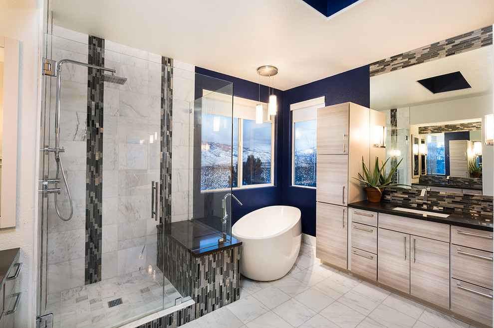Example of a trendy master beige tile and porcelain tile porcelain tile and beige floor freestanding bathtub design with flat-panel cabinets, brown cabinets, blue walls, an undermount sink and a hinged shower door