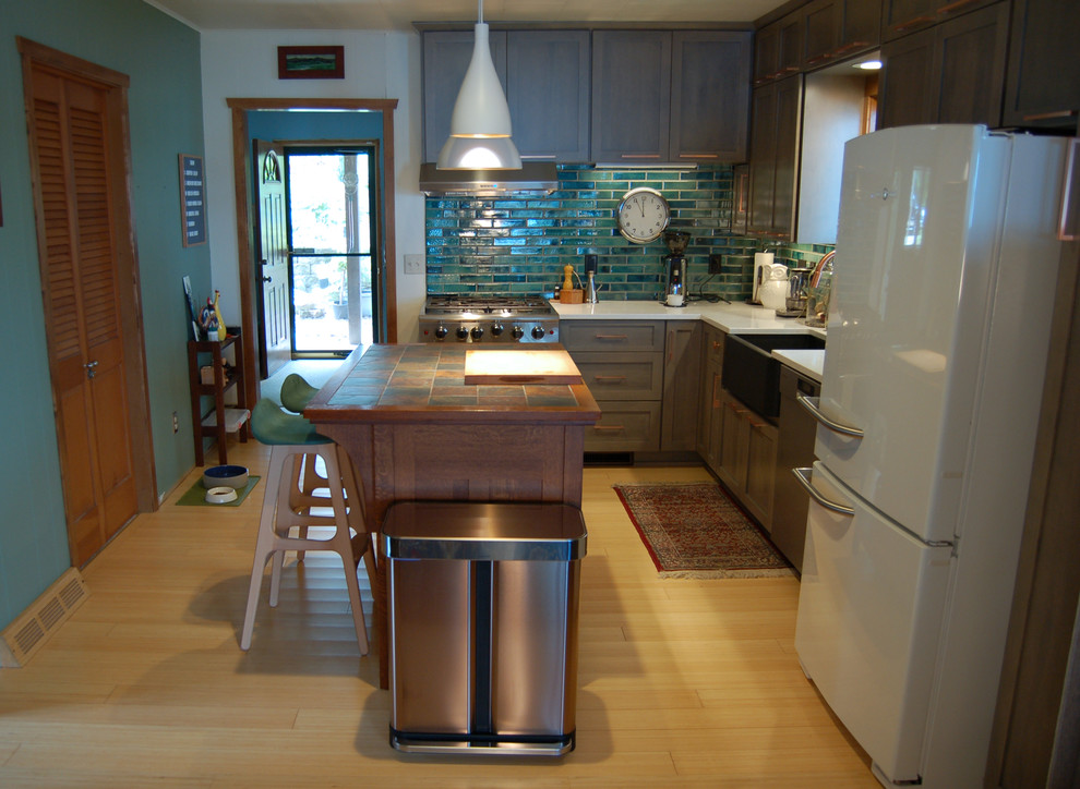 Open concept kitchen - transitional l-shaped light wood floor and multicolored floor open concept kitchen idea with a farmhouse sink, shaker cabinets, gray cabinets, quartzite countertops, blue backsplash, ceramic backsplash, stainless steel appliances and an island