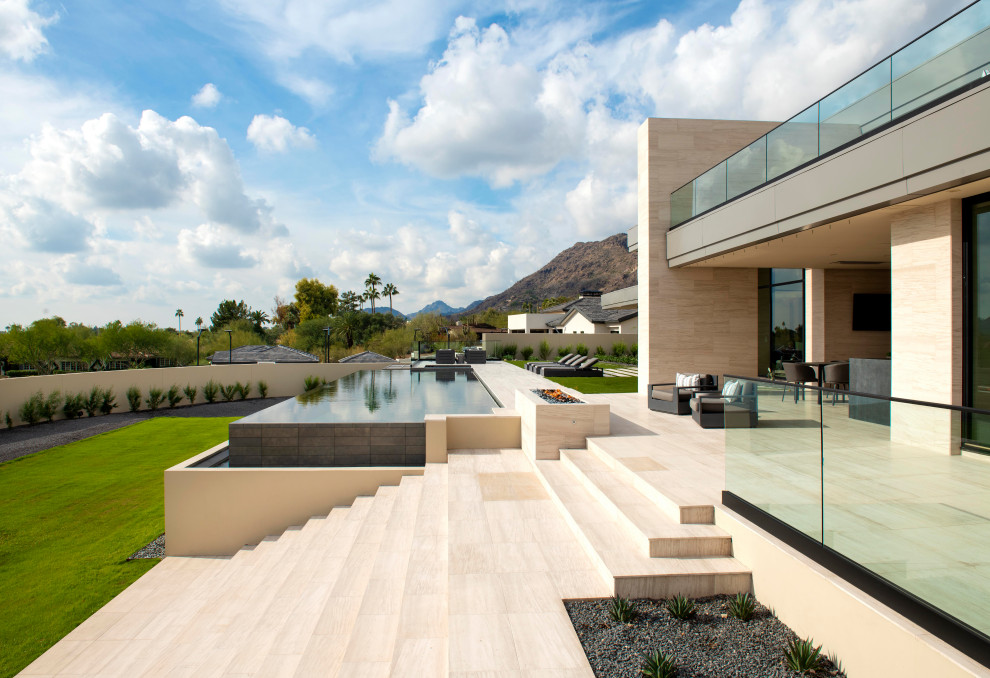 This is an example of an expansive contemporary back rectangular infinity swimming pool in Phoenix with with pool landscaping and natural stone paving.