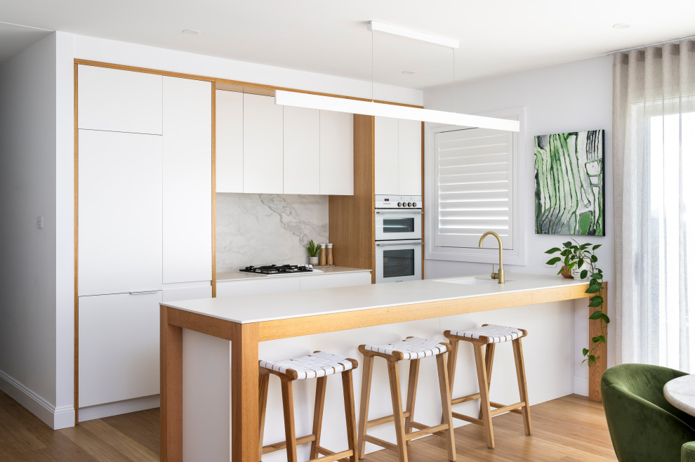 Photo of a mid-sized beach style galley eat-in kitchen in Newcastle - Maitland with an undermount sink, quartz benchtops, stone slab splashback, laminate floors and with island.
