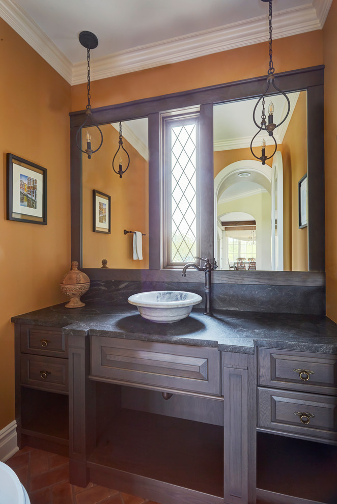 This is an example of a small traditional powder room in Chicago with raised-panel cabinets, dark wood cabinets, orange walls, ceramic floors, a vessel sink, granite benchtops, red floor, black benchtops and a one-piece toilet.