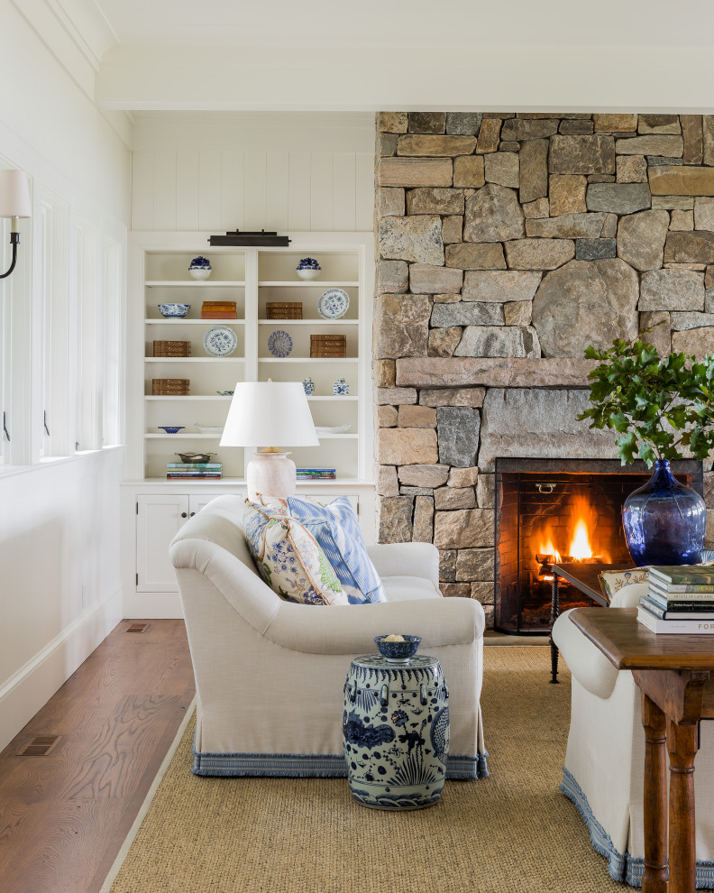 Inspiration for a beach style open concept living room in Boston with a library, white walls, medium hardwood floors, a standard fireplace, a stone fireplace surround, no tv, brown floor and planked wall panelling.