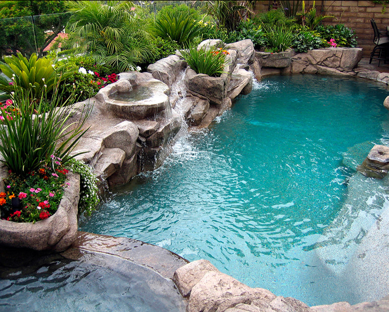 Design ideas for a mid-sized tropical backyard custom-shaped pool in Orange County with a water slide and stamped concrete.