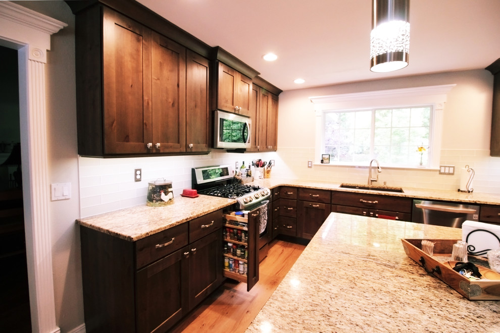 Inspiration for a large rustic u-shaped light wood floor and brown floor open concept kitchen remodel in Boise with an undermount sink, shaker cabinets, brown cabinets, granite countertops, white backsplash, glass tile backsplash, stainless steel appliances and an island