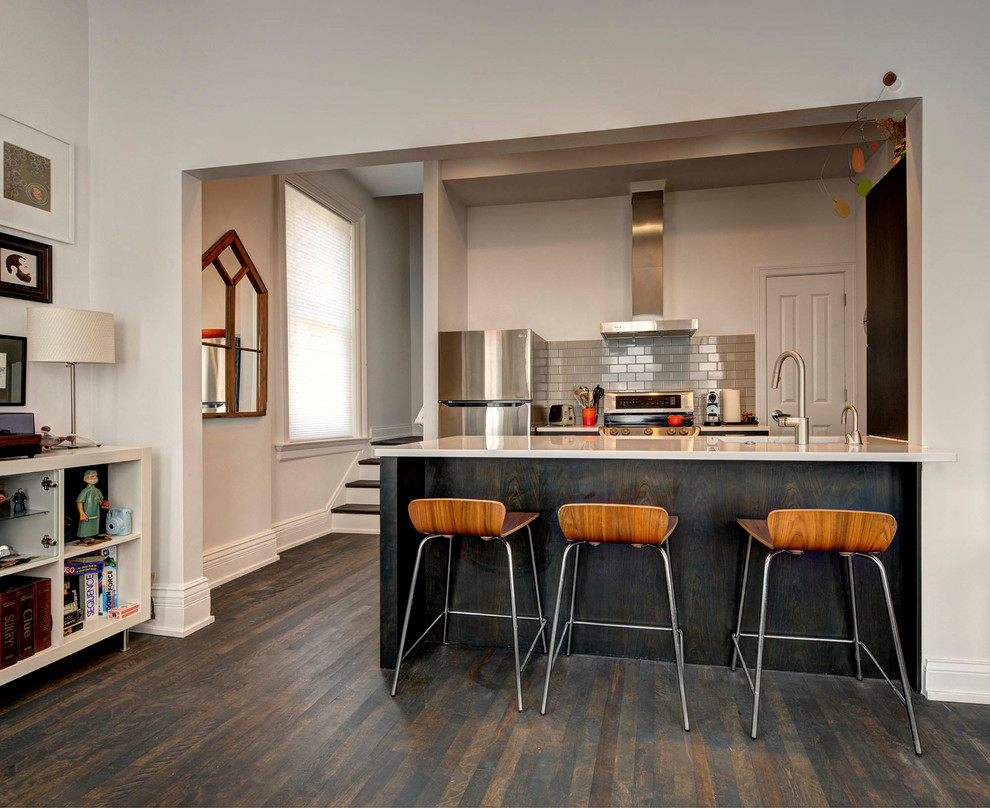 Photo of a small industrial single-wall eat-in kitchen in Cincinnati with an undermount sink, flat-panel cabinets, black cabinets, quartzite benchtops, grey splashback, ceramic splashback, stainless steel appliances, dark hardwood floors, a peninsula, brown floor and white benchtop.