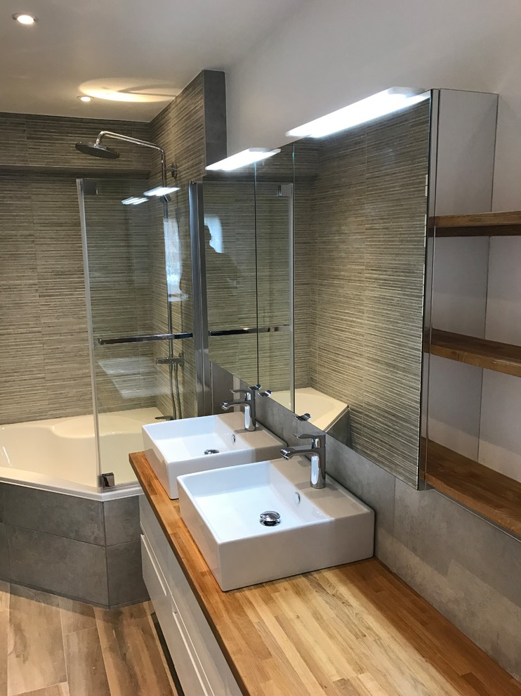 Inspiration för små moderna en-suite badrum, med ett hörnbadkar, grå kakel, grå väggar, ett nedsänkt handfat, träbänkskiva och brunt golv