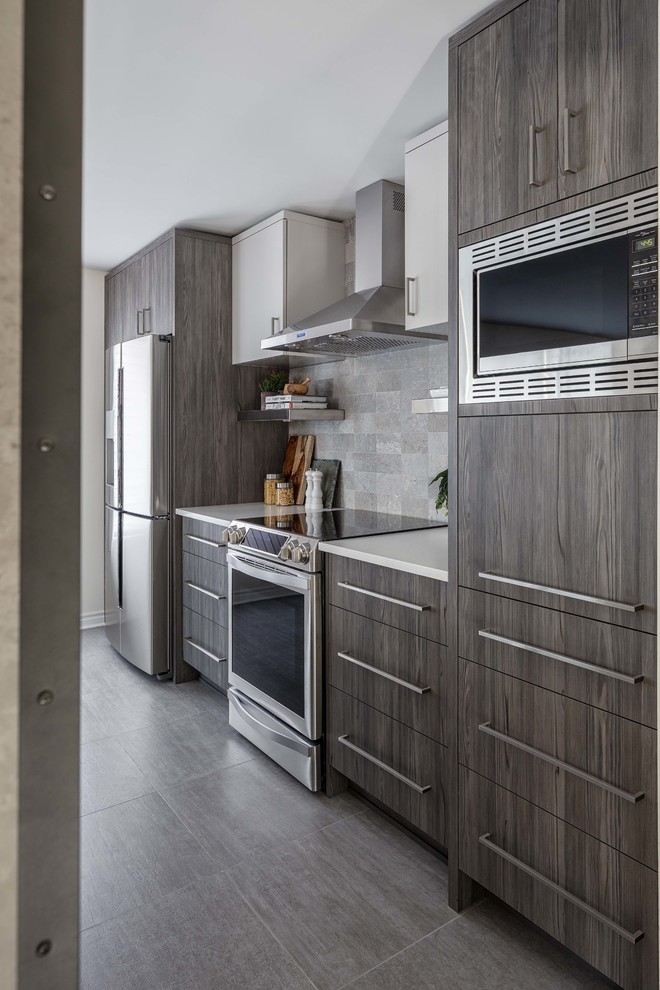 Mid-sized industrial single-wall eat-in kitchen in Ottawa with an integrated sink, flat-panel cabinets, medium wood cabinets, quartzite benchtops, grey splashback, subway tile splashback, stainless steel appliances, ceramic floors, with island and grey floor.