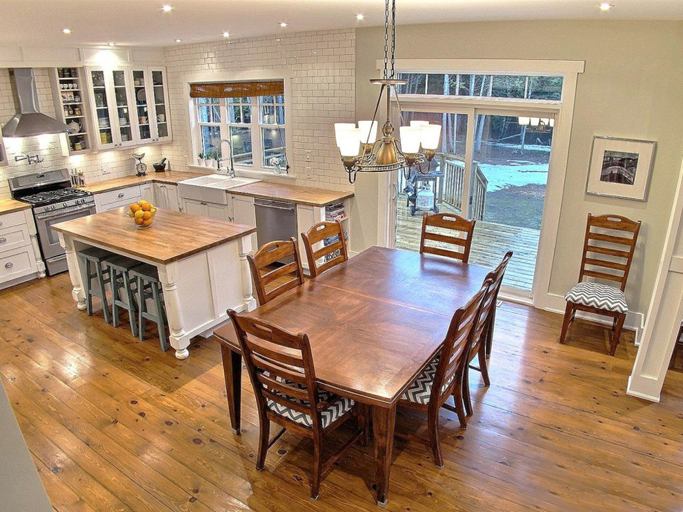 Large transitional u-shaped medium tone wood floor open concept kitchen photo in Ottawa with a farmhouse sink, shaker cabinets, distressed cabinets, wood countertops, white backsplash, subway tile backsplash, stainless steel appliances and an island