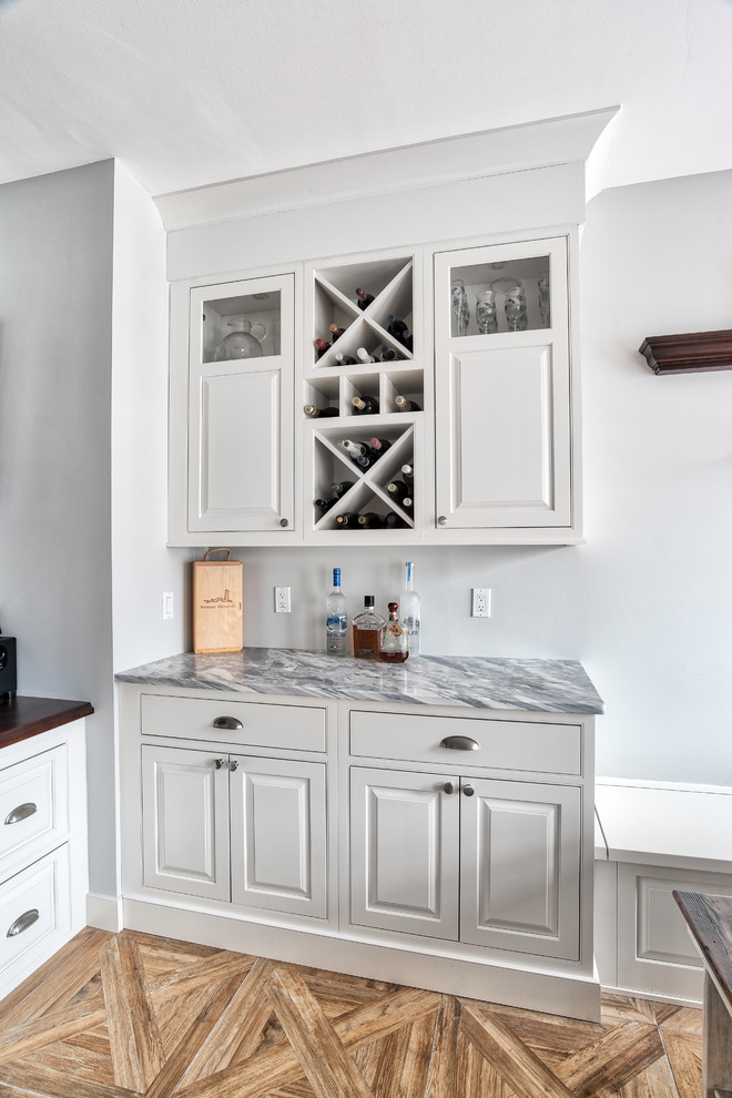 Photo of a small country single-wall home bar in New York with beaded inset cabinets, white cabinets, marble benchtops, ceramic floors and brown floor.