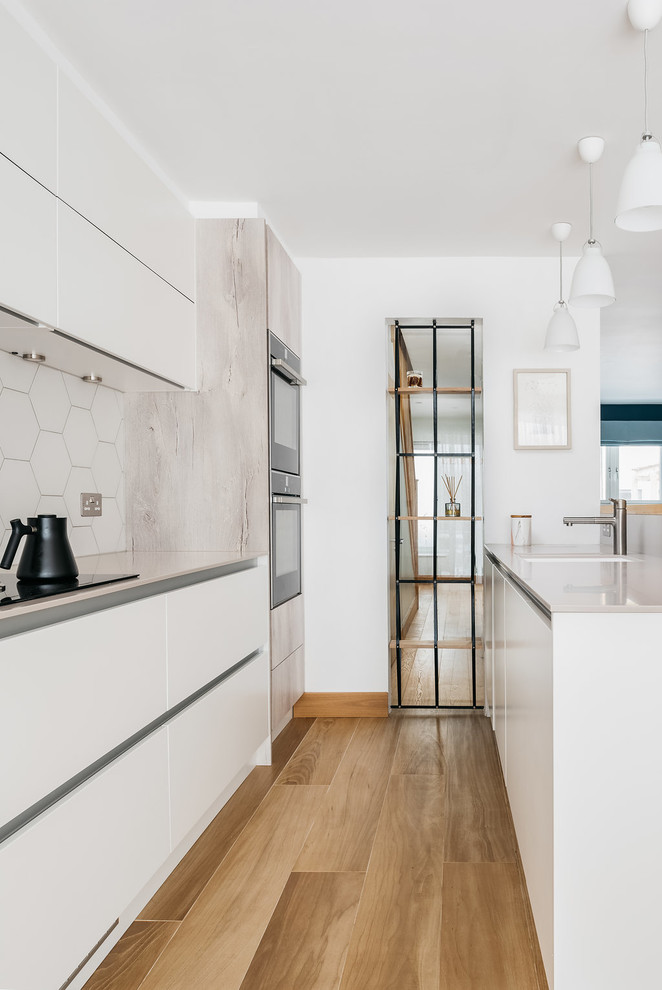 Photo of a large scandinavian single-wall open plan kitchen in Cambridgeshire with an undermount sink, flat-panel cabinets, light wood cabinets, quartz benchtops, white splashback, ceramic splashback, panelled appliances, ceramic floors, a peninsula and brown floor.