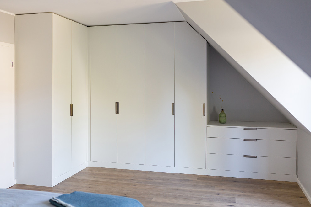 Large scandinavian women's dressing room in Cologne with flat-panel cabinets, white cabinets, medium hardwood floors, brown floor and wallpaper.