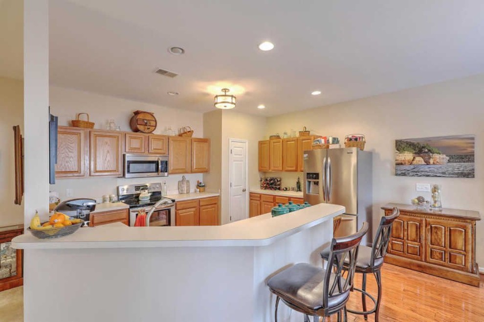 Example of a mid-sized u-shaped medium tone wood floor and brown floor kitchen design in Charleston with an undermount sink, raised-panel cabinets, beige cabinets, granite countertops, brown backsplash, ceramic backsplash, stainless steel appliances and beige countertops