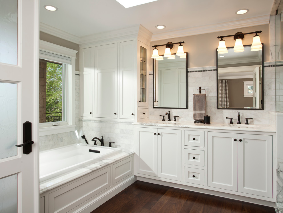 Photo of a mid-sized traditional master bathroom in Salt Lake City with recessed-panel cabinets, white cabinets, a drop-in tub, white tile, beige walls, dark hardwood floors, marble, an undermount sink, marble benchtops and brown floor.