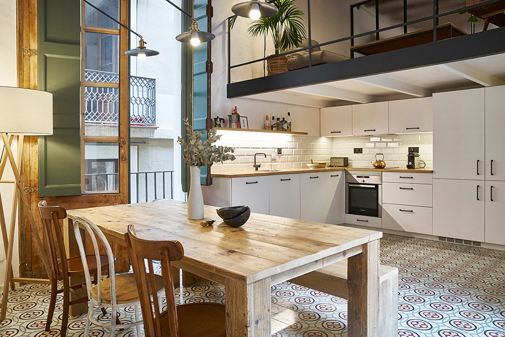 This is an example of a mediterranean l-shaped eat-in kitchen in Barcelona with flat-panel cabinets, white cabinets, wood benchtops, white splashback, subway tile splashback, no island, a single-bowl sink, stainless steel appliances and multi-coloured floor.